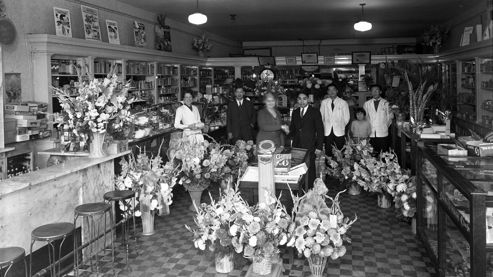 Shows a busy shop filled with elaborate arrangements and well-dressed staff.