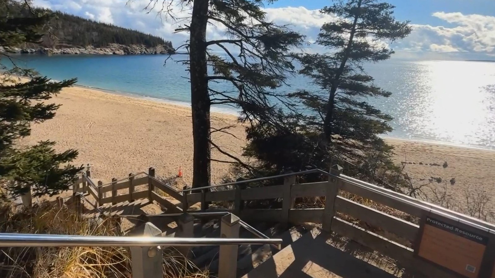 A steep outdoor stairwell with metal handrails that leads down to a vast beach with open ocean
