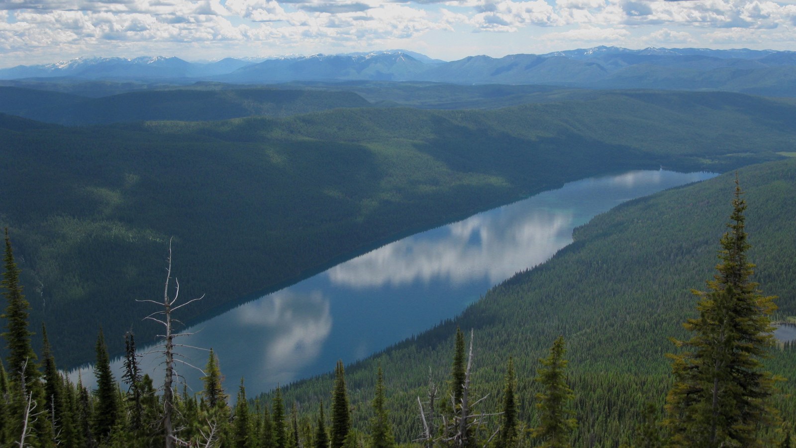 A long lake nestled between sloping and forested mountainsides. 