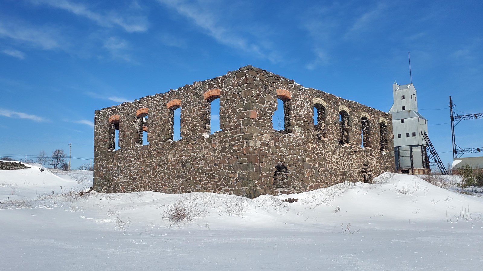 Winter scene of poor-rock building ruin with brick-arch-topped windows and rough arched entrance.