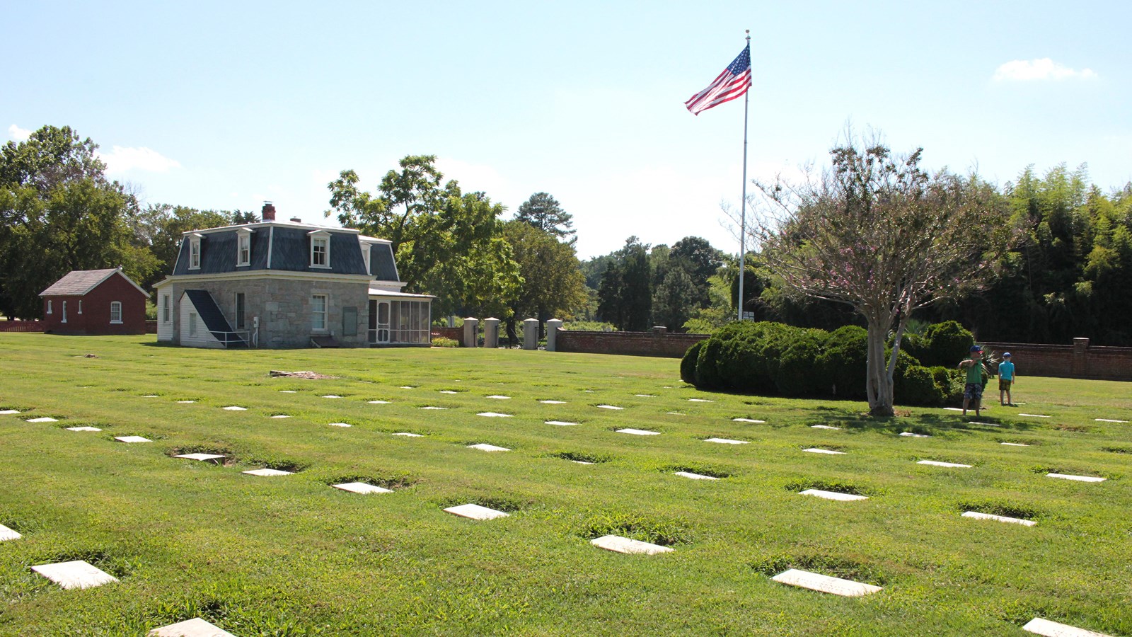 A grey house is in the background with an American Flag on a pole. Grave markers are in foreground