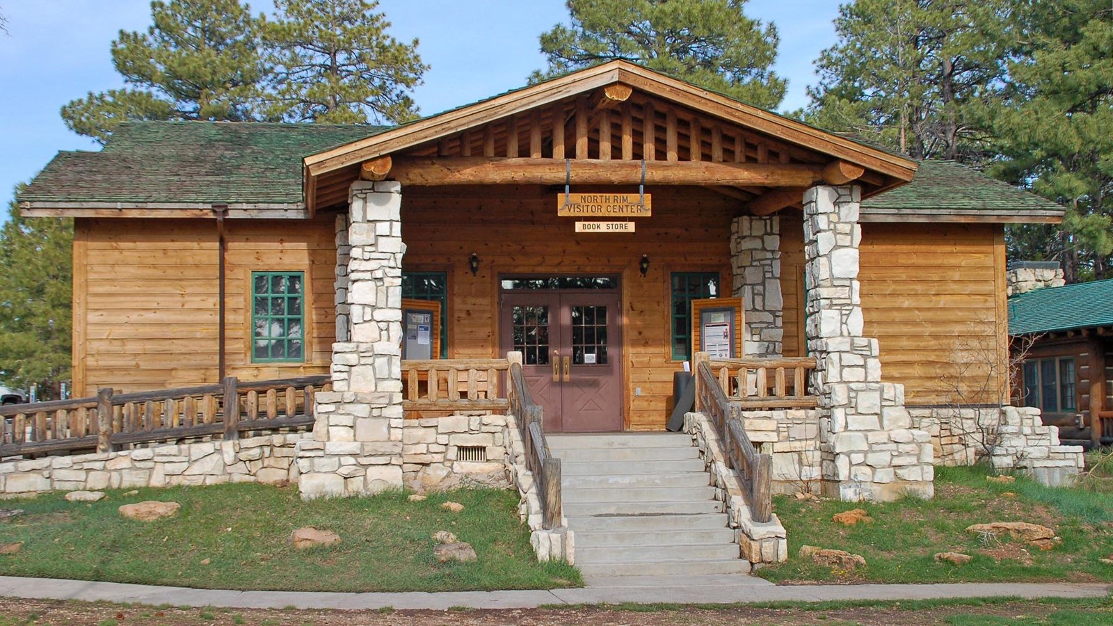 Paved stairs lead to a light brown wooden building with a green roof and large white stone columns. 