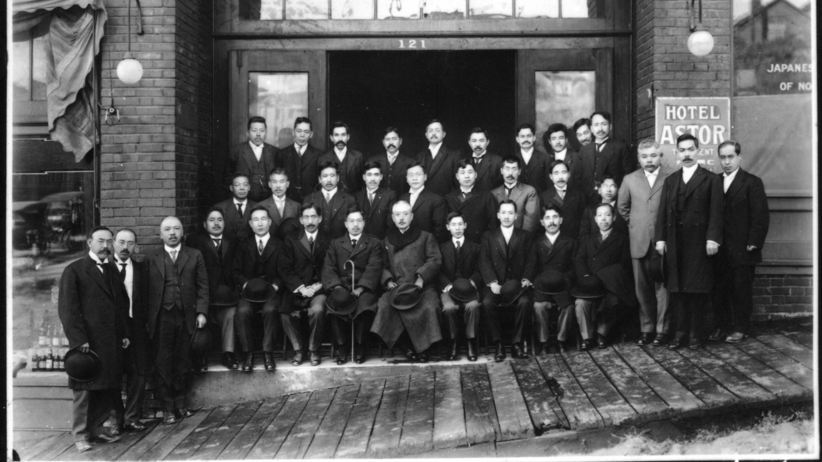 This black-and-white photograph showcases a group of men posing in front of a brick building.