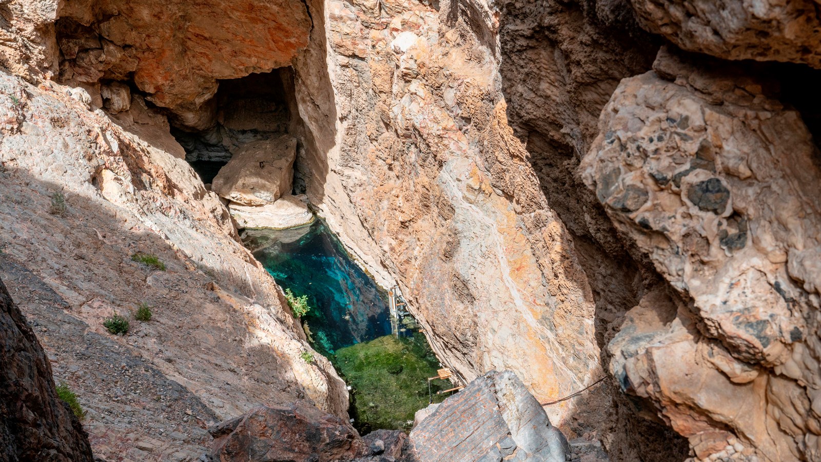 Steep rocky cliffs rise up on 3 sides from the teal water of a pool containing research equipment.  