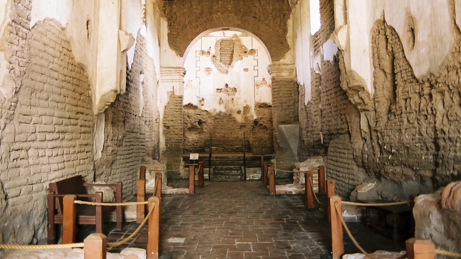 interior view of long hall of church with partially plastered adobe walls