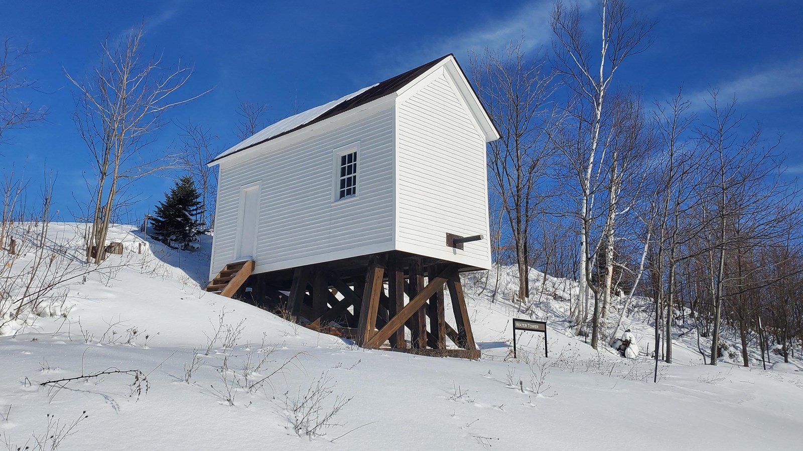 Winter scene of white building with large wood beams underneath and wooden stairs leading to a door.