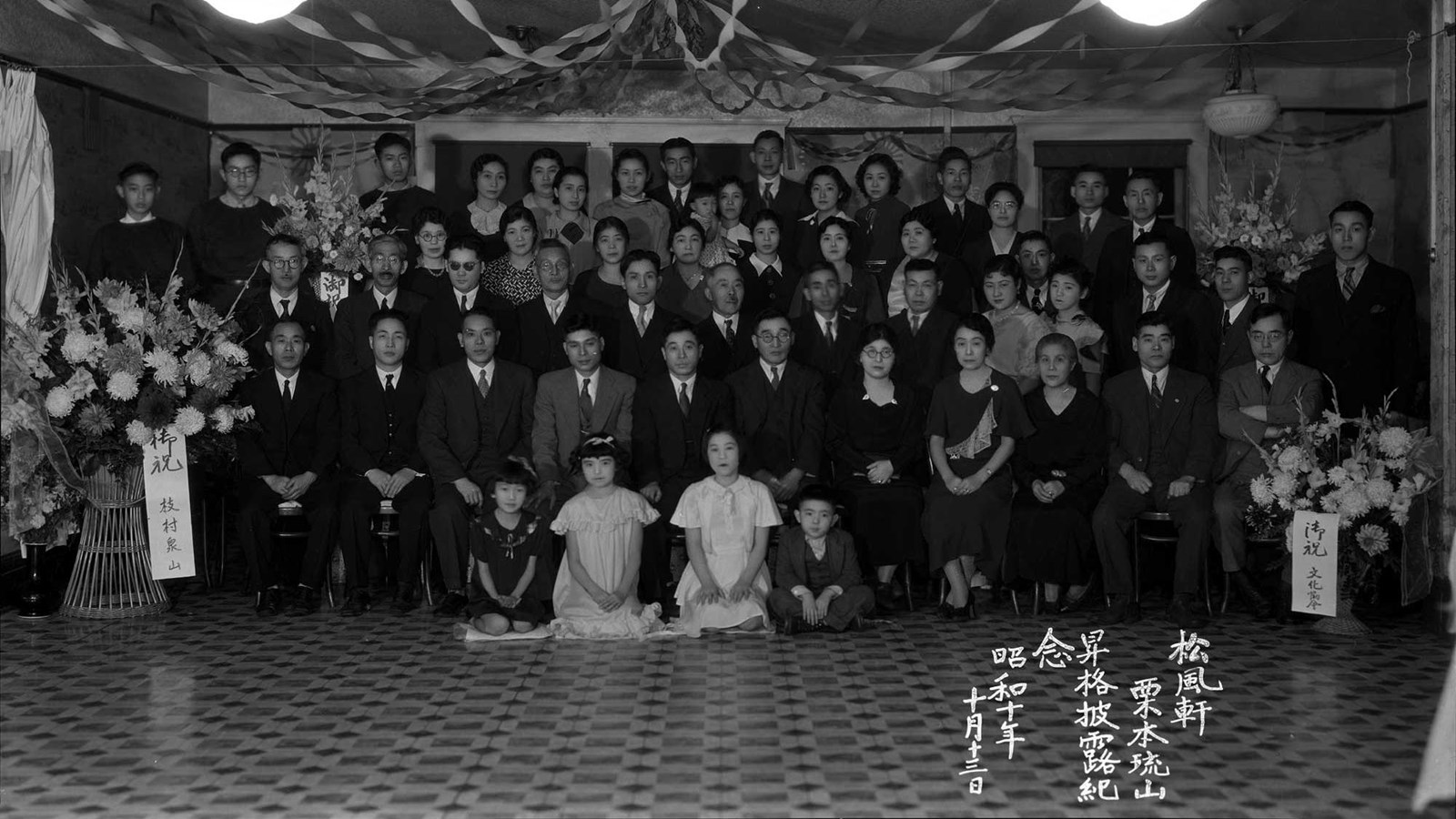 Black-and-white photograph depicts a formal gathering of adults and children, arranged in four rows.