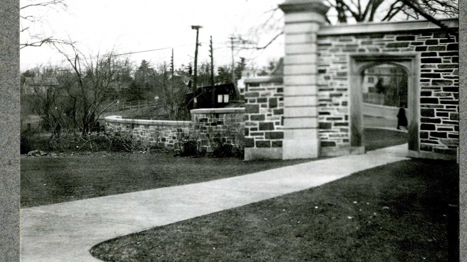 Black and white of path going through stone arch on flat grassy area 