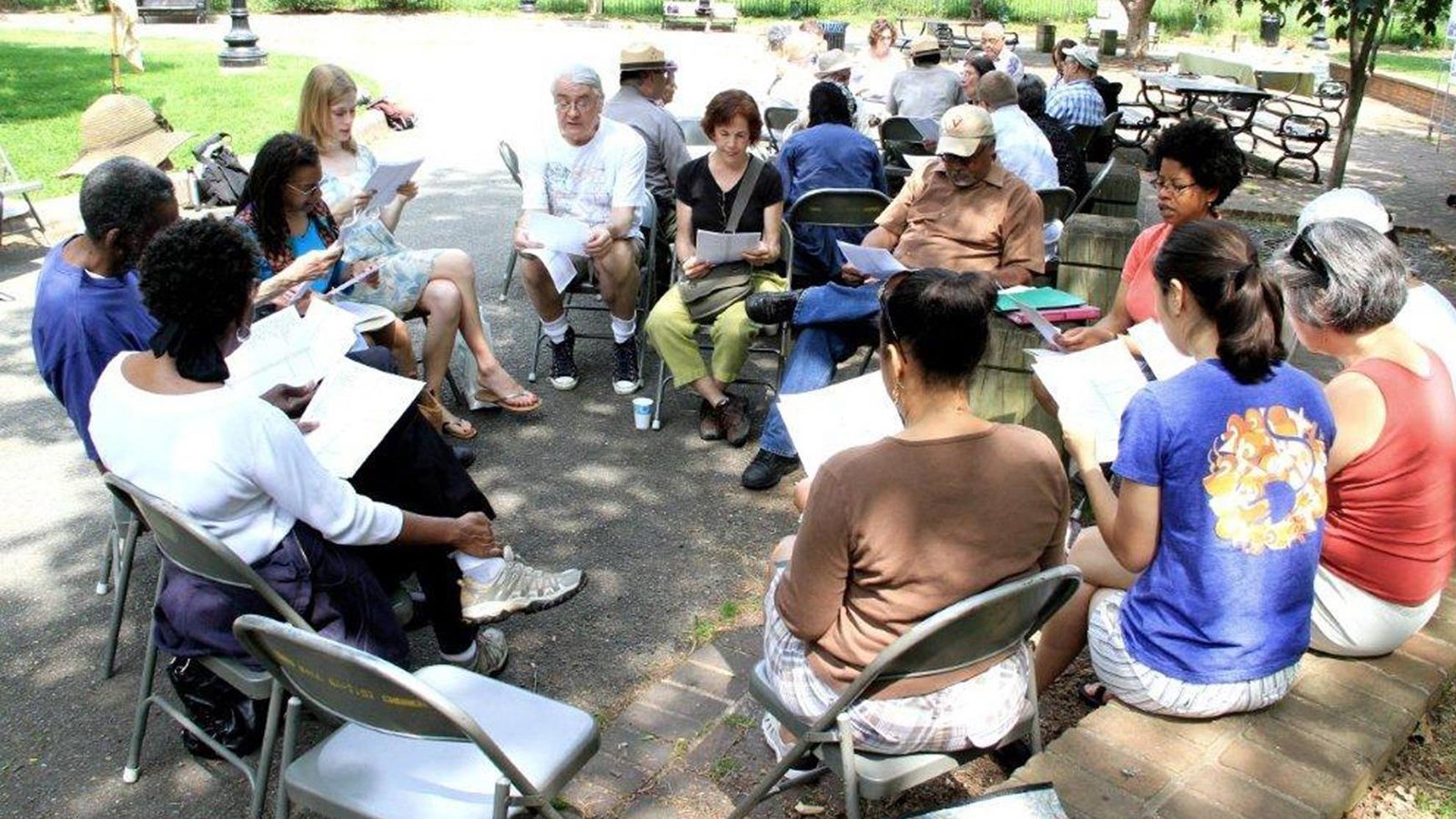 Groups of people sit in circles of chairs viewing pieces of paper.