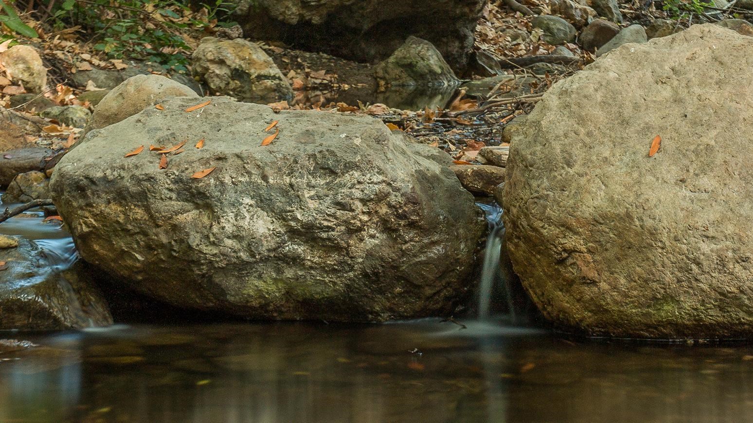 A stream of water falling from in between two rocks into a creek.