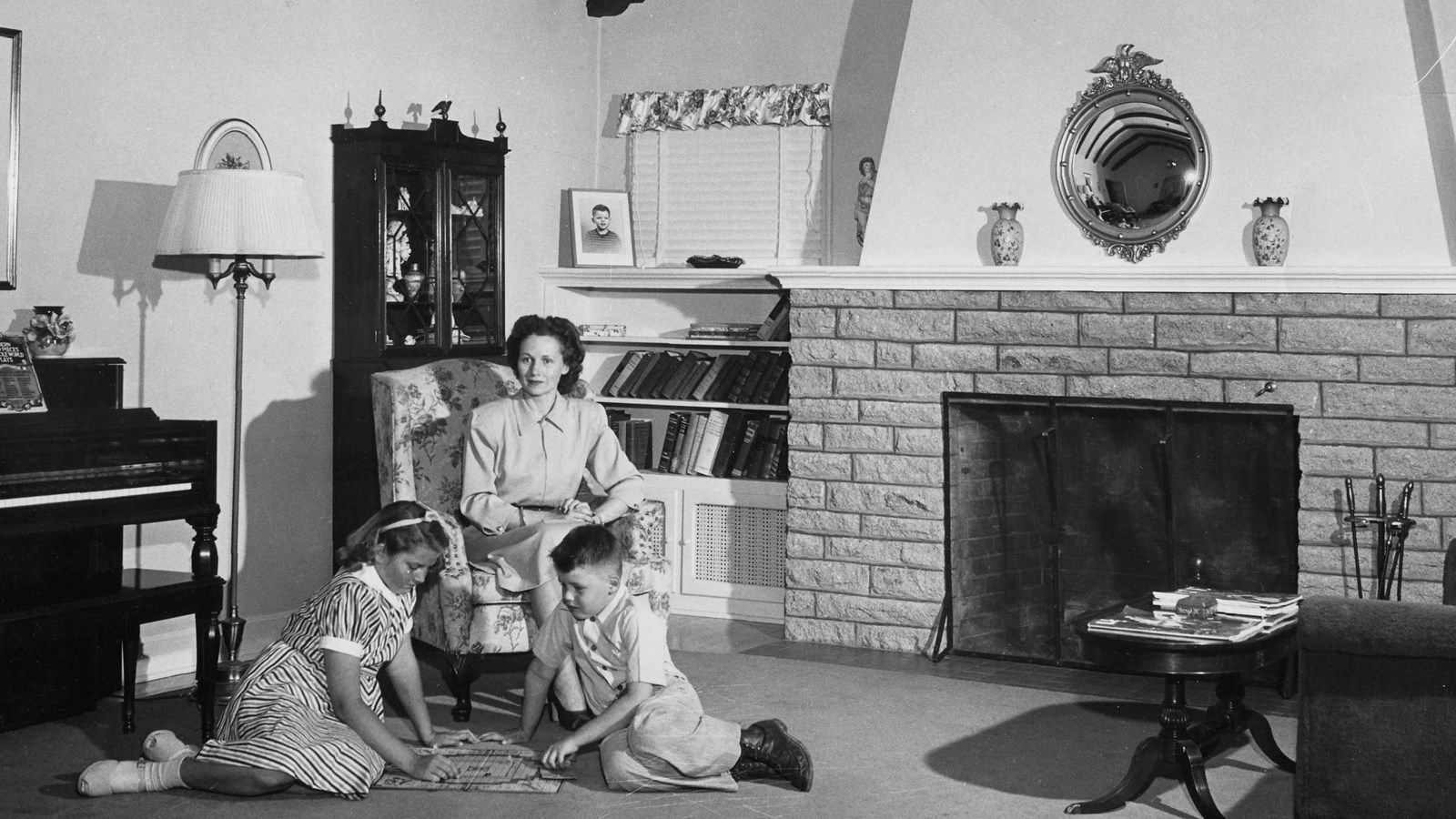 Nellie Warren sits in a chair, while her two kids Patricia, and Conrad play a board game.