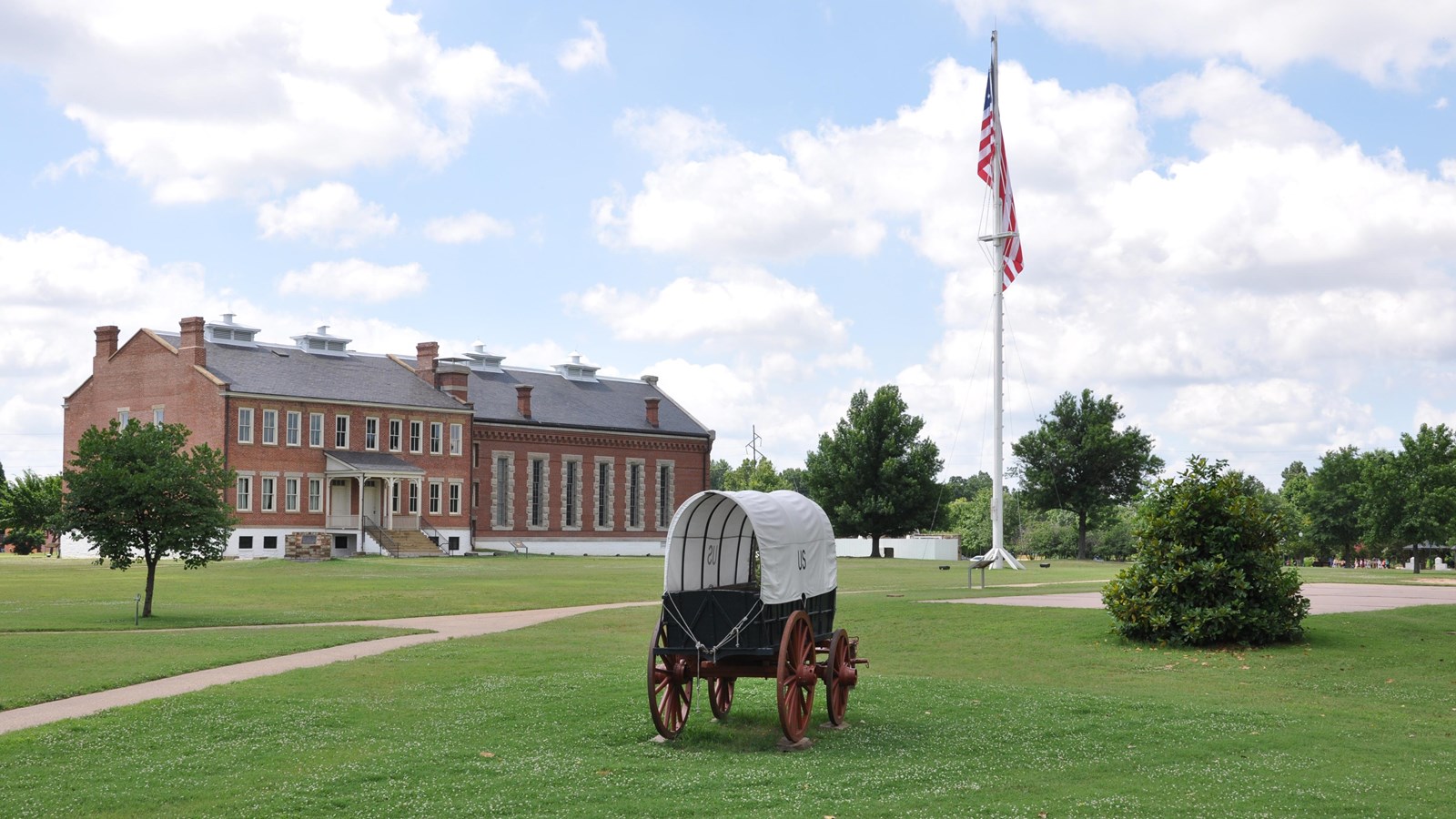 A blue supply wagon with a canvas cover in front of the red brick visitor center and white flagpole.