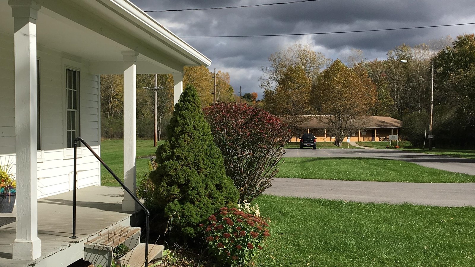 A white building with a large porch and a building in the distance