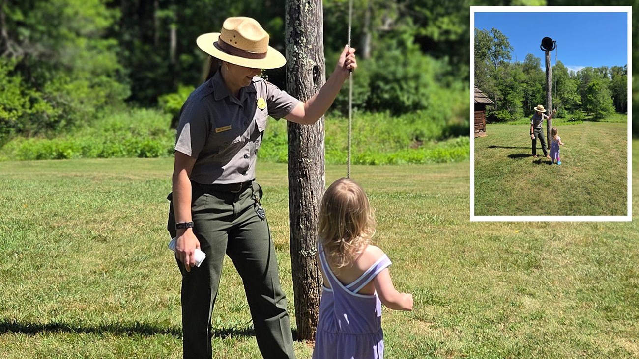 A park ranger stands beside a wooden pole and demonstrates to a small child how to ring the bell. 