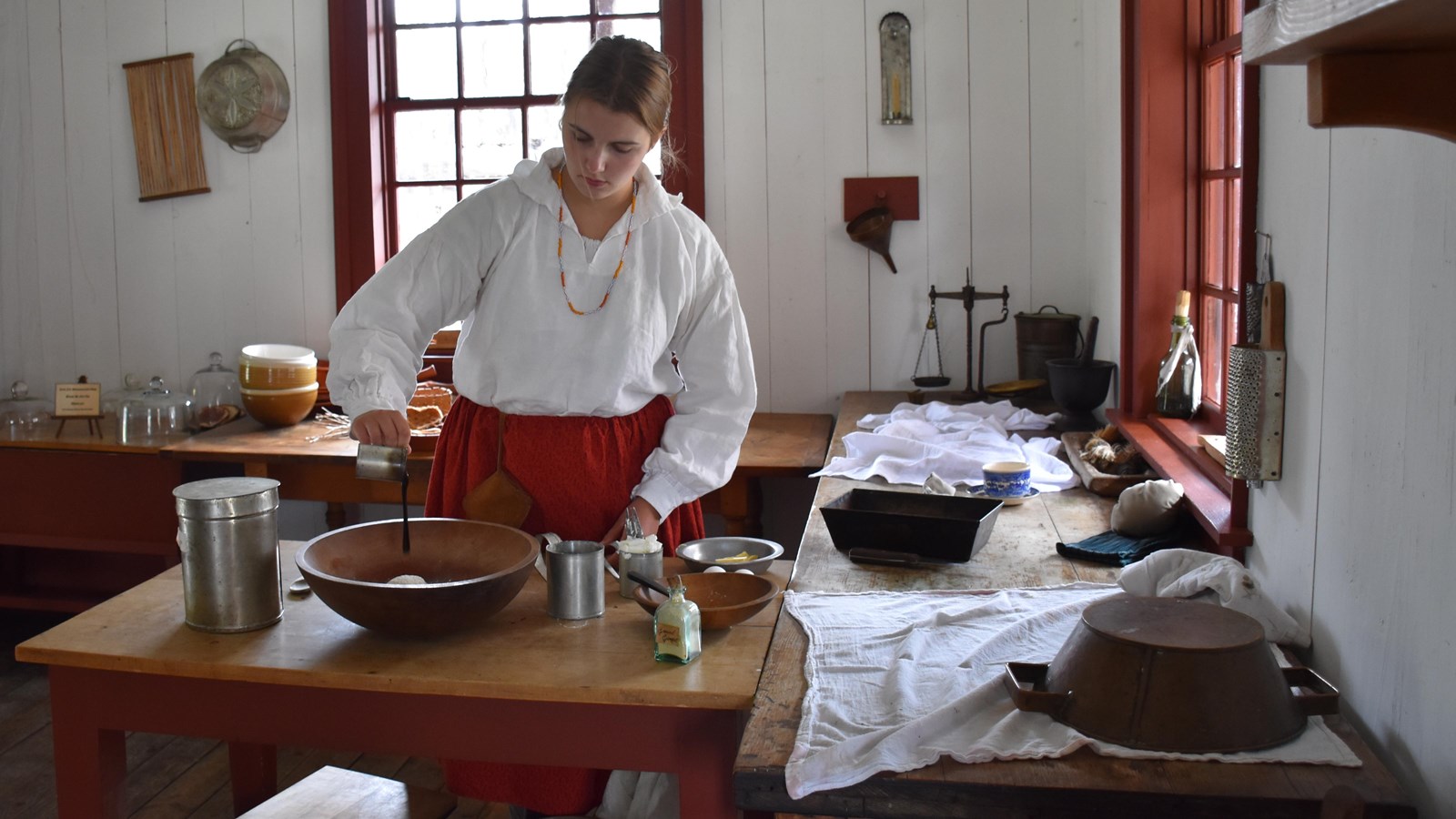 A person pours molasses into a mixing bowl on a table with other ingredients.