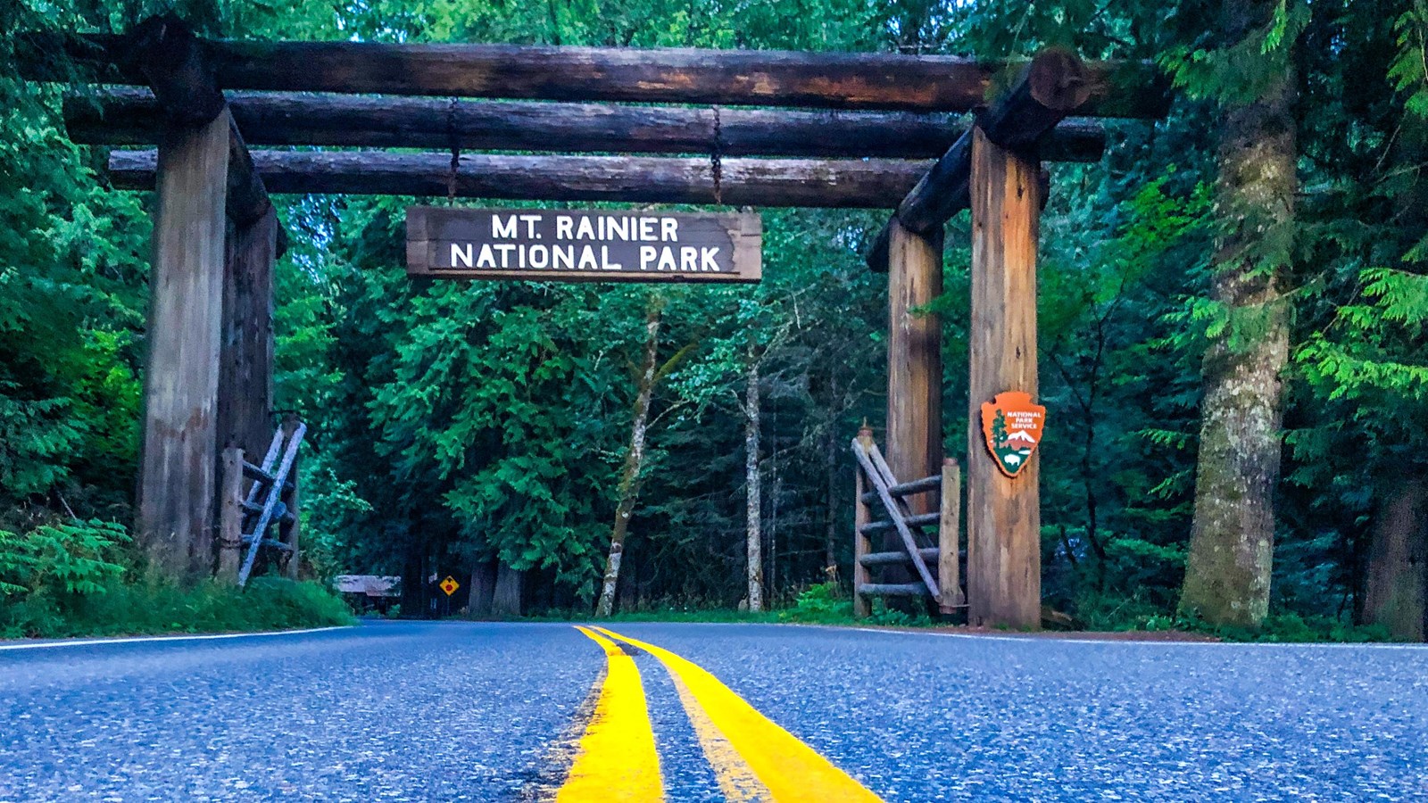 The road leads to a massive log archway with a sign that reads, 