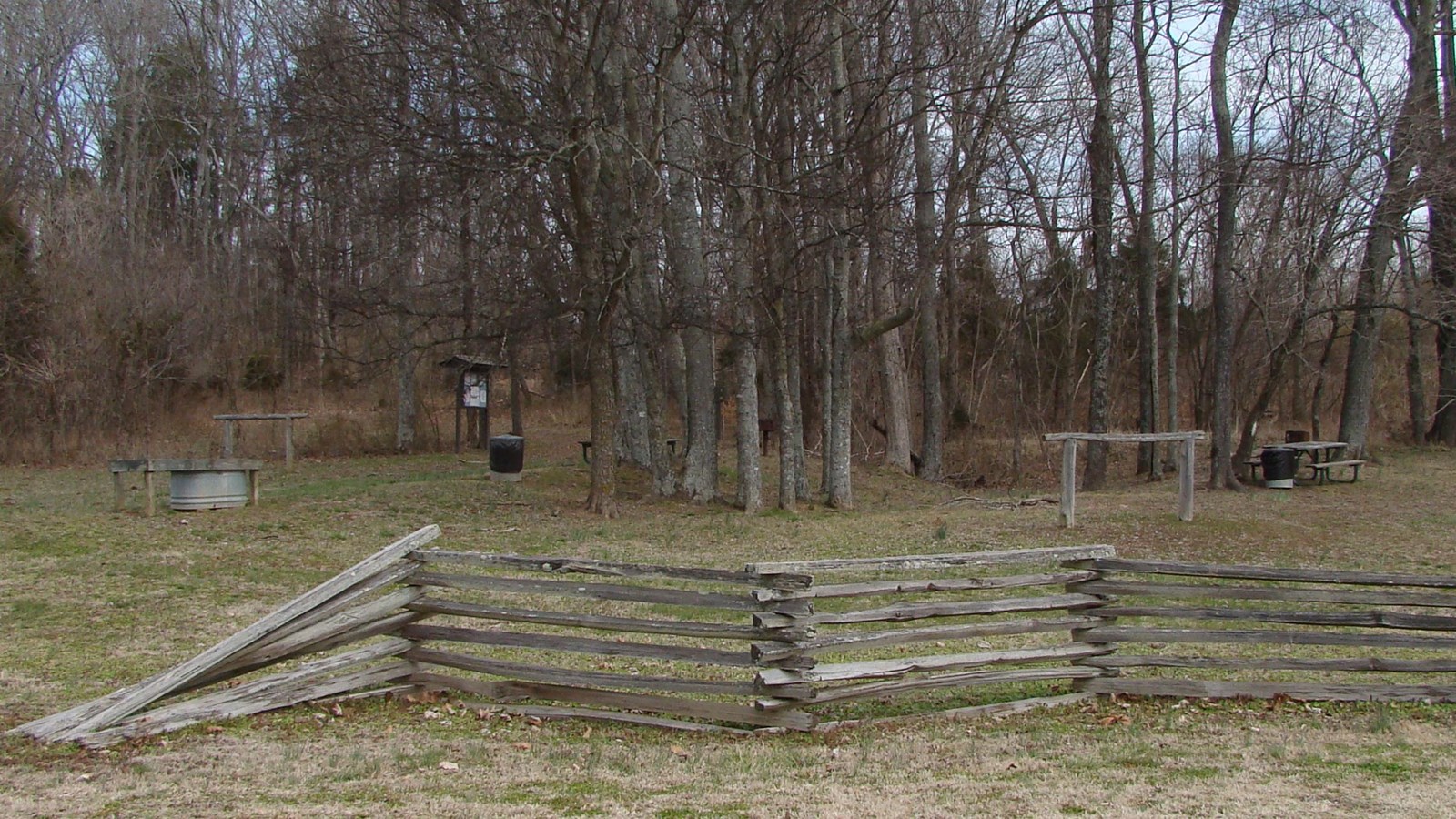 Hiking trailhead with wooden fence in foreground. Table and hitching post behind fence.