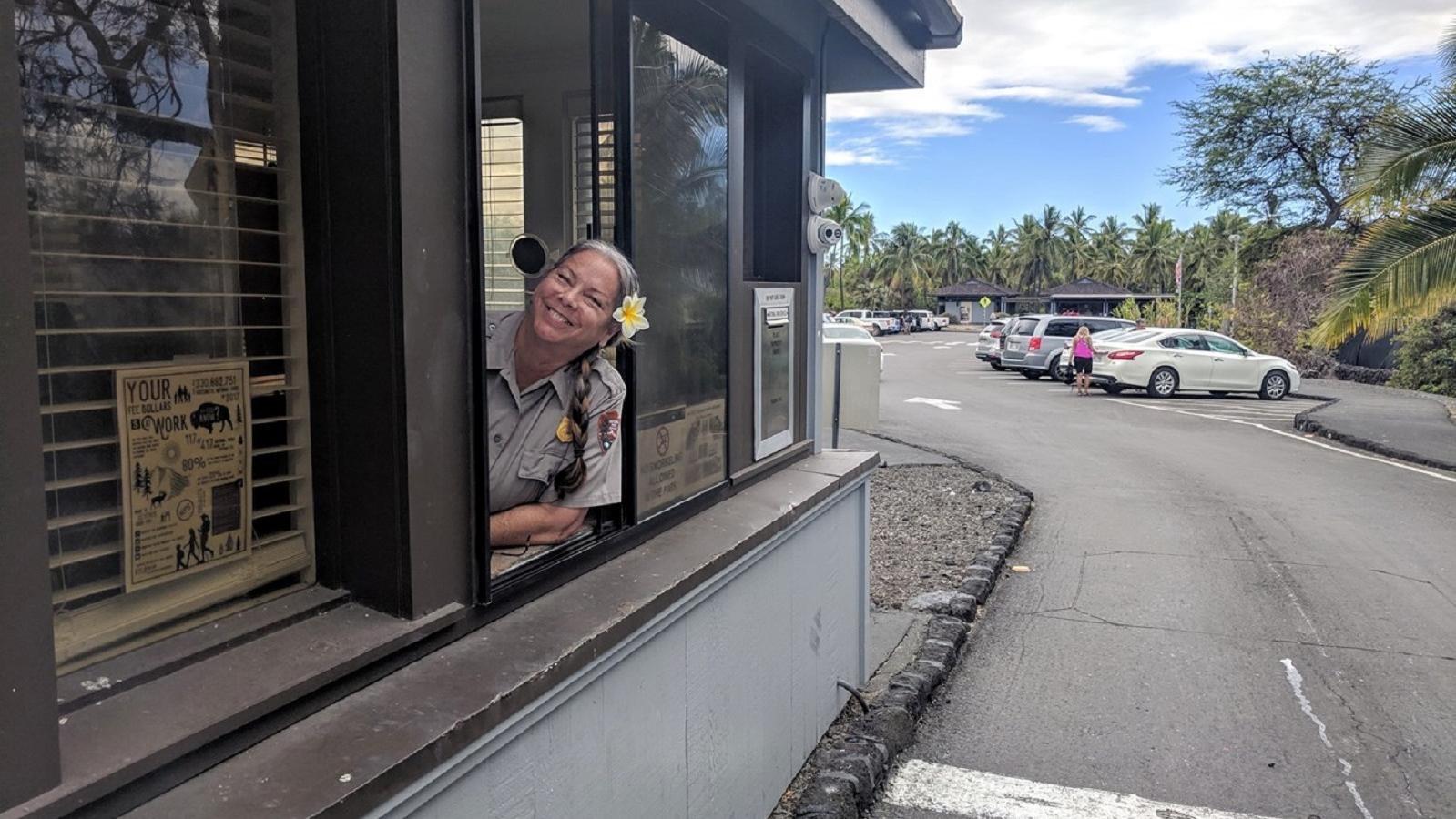 A ranger with a flower in her hair sitting in the entrance station booth.