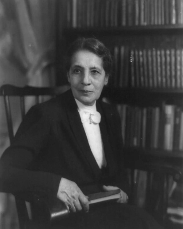 Black and white photo of a woman sitting in a chair with a bookshelf behind her.