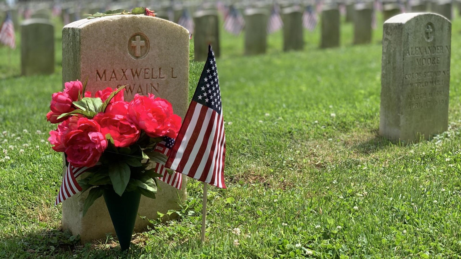 white grave stone with red flowers and American flag on each side