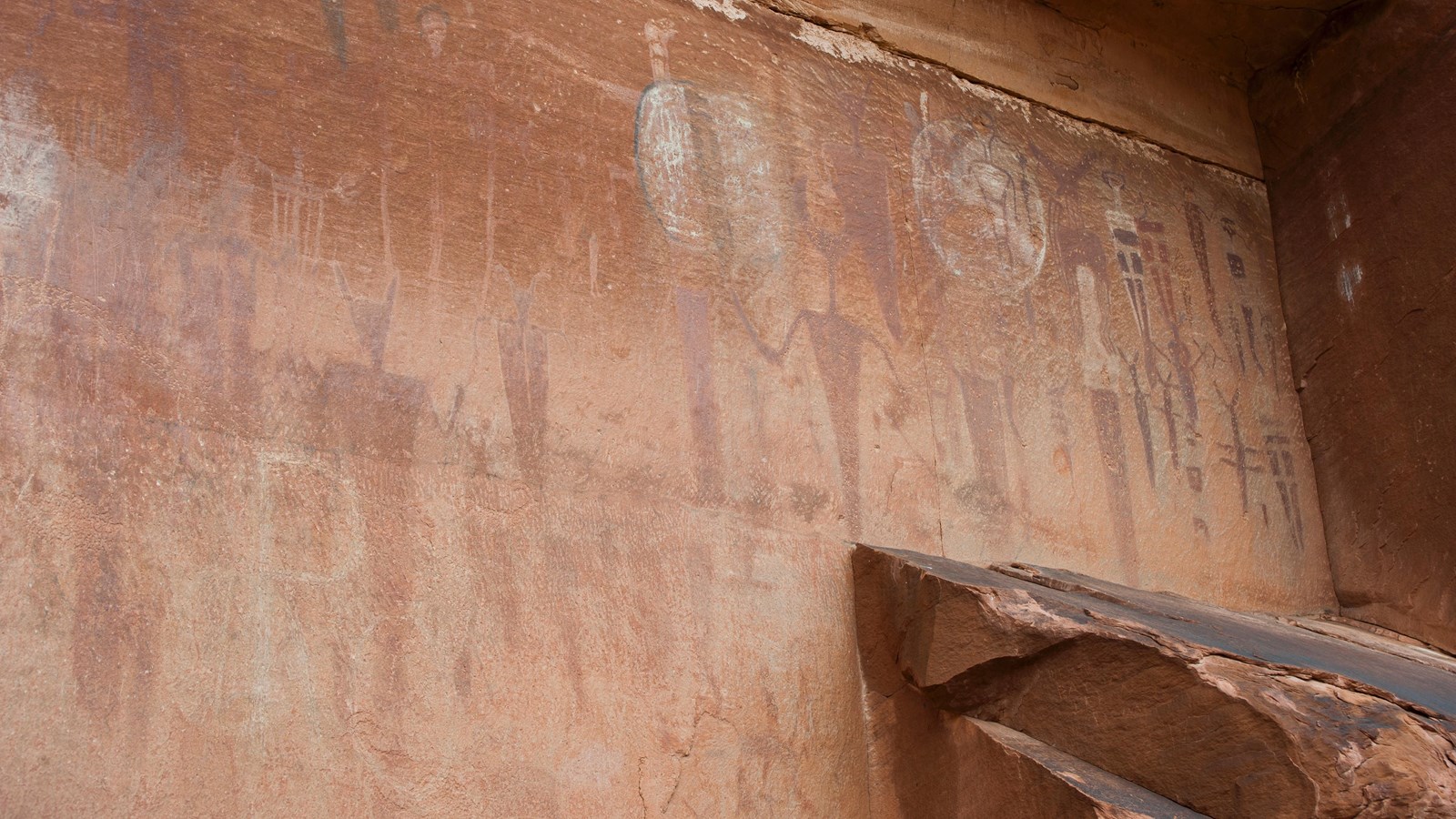 Faint red, white, & brown painted markings of tapered human figures on a sandstone wall