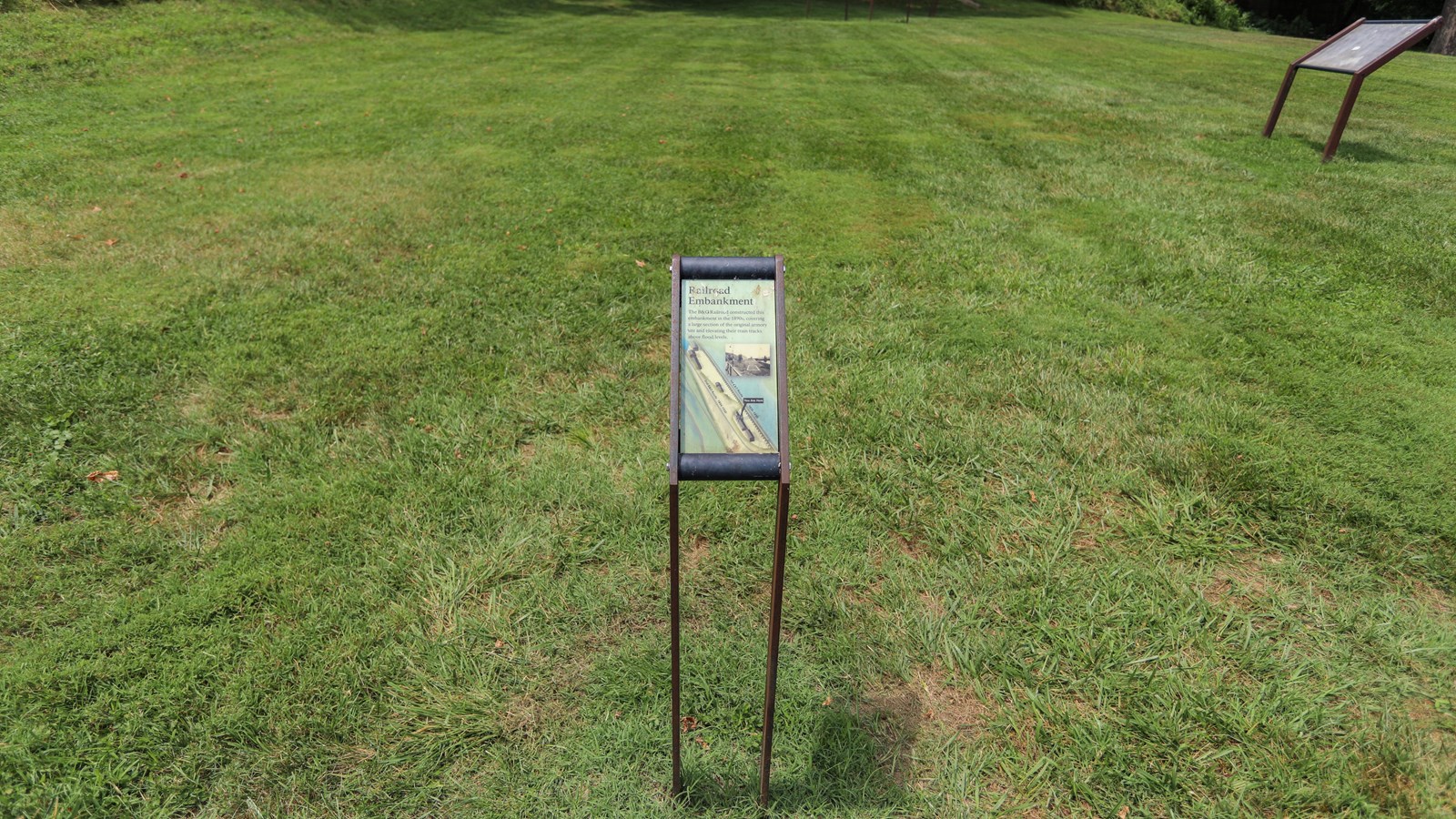 A tall informational panel in front of a grassy field. 