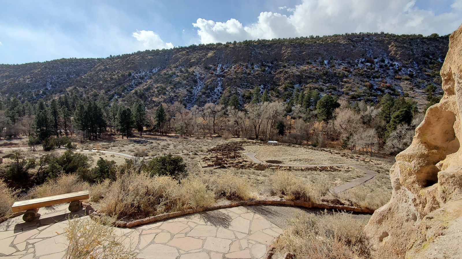 a wooden bench sits overlooking the remnants of a stone structure in the bottom of a canyon
