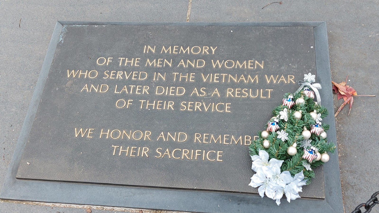 Rectangular bronze plaque on stone plaza with small Christmas tree next to it