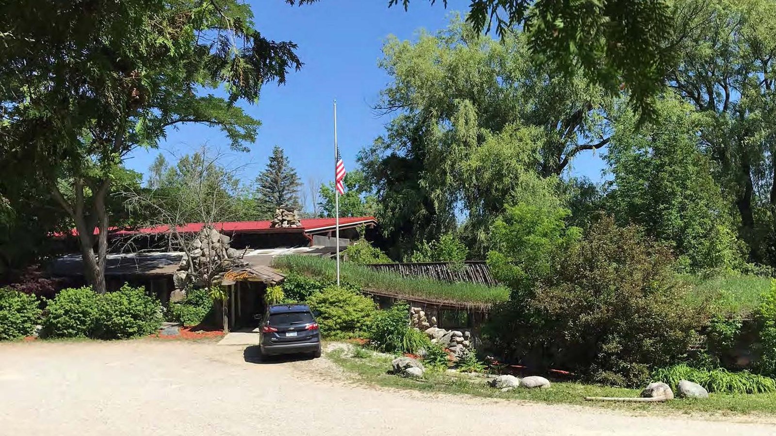 A two story building with red roof set into hillside within a wooded area. 