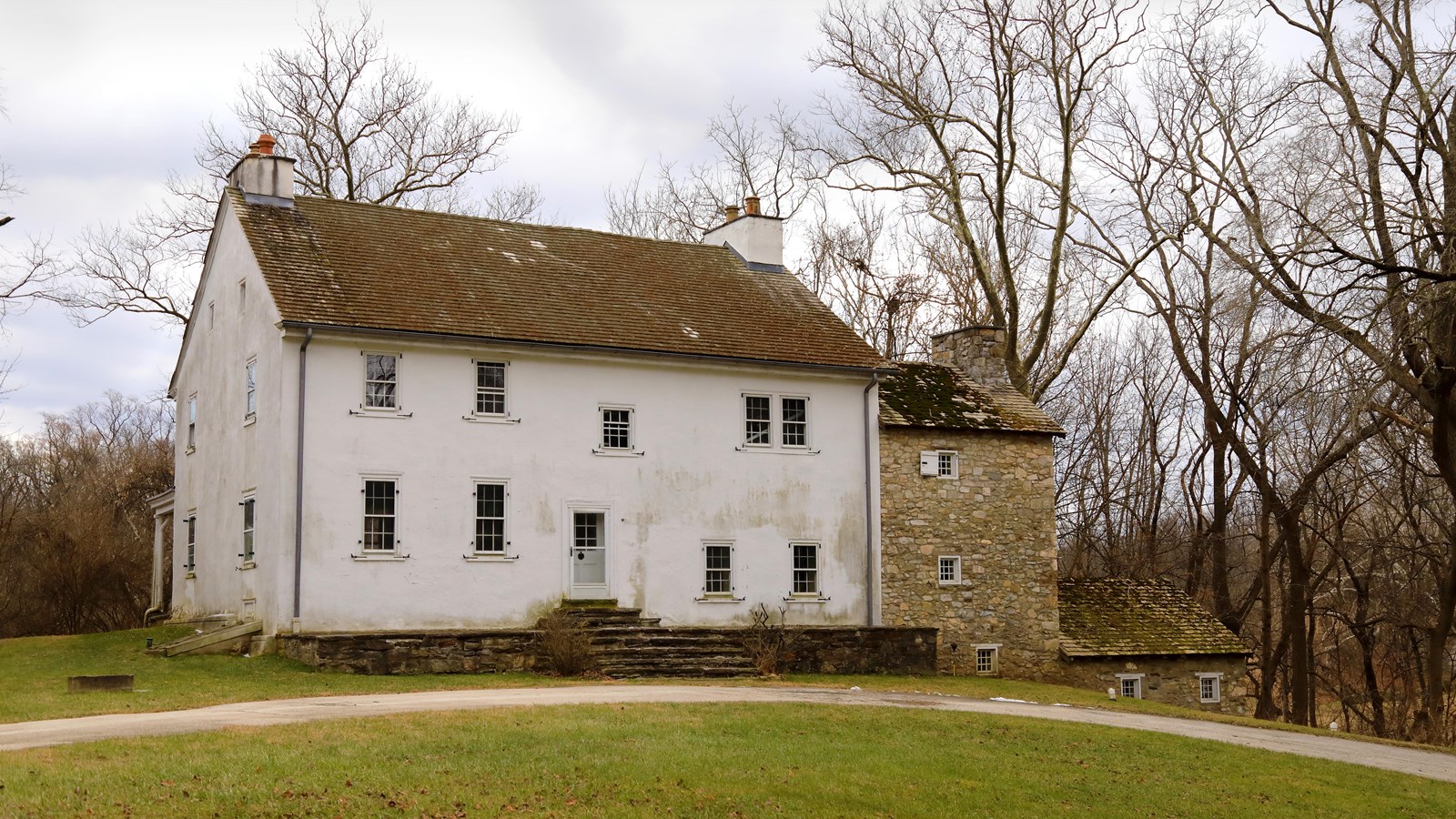 a two-story farmhouse with white siding and an older stone section on the right side