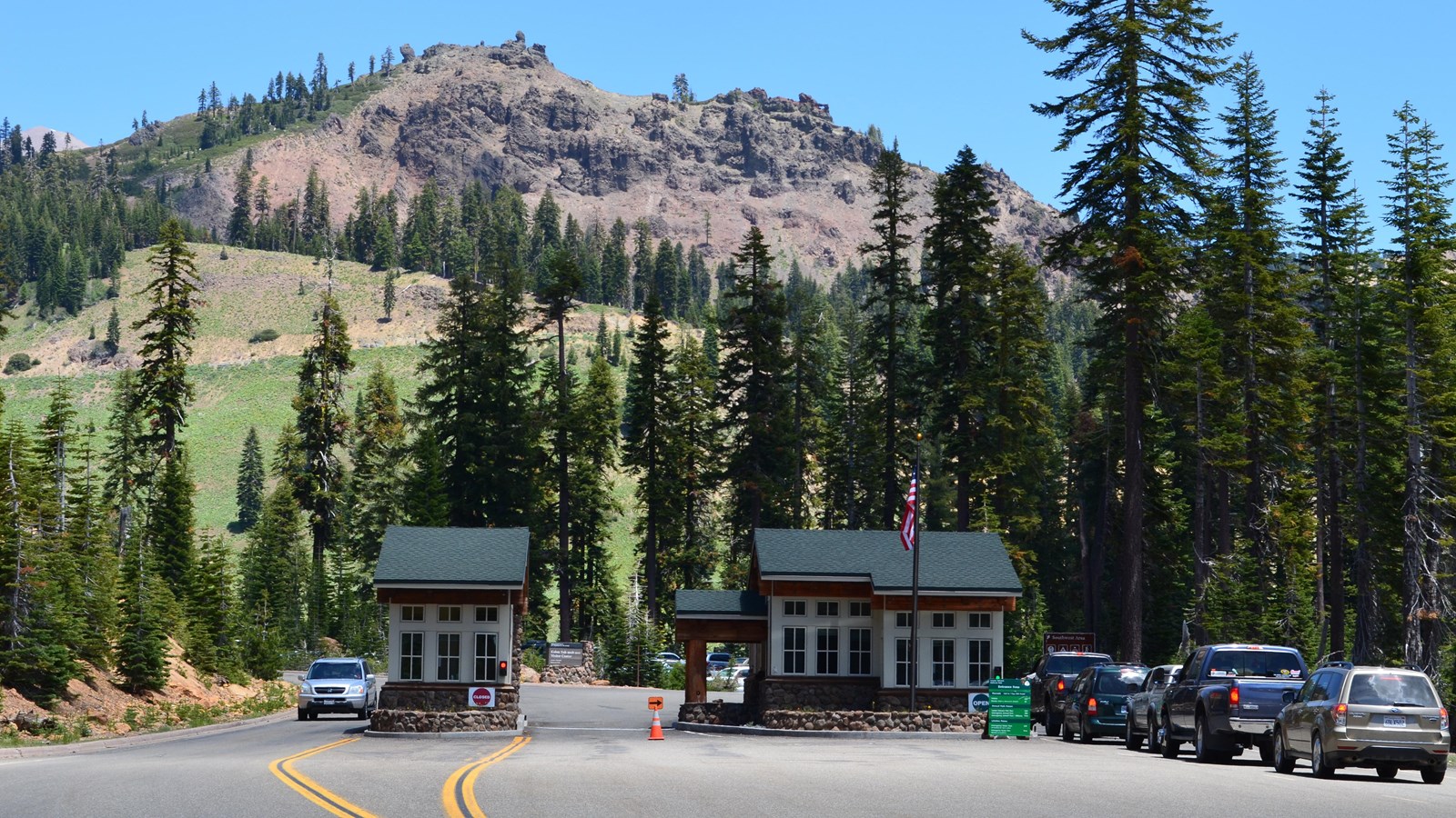 cars lined up next to a fee booth, mountains behind