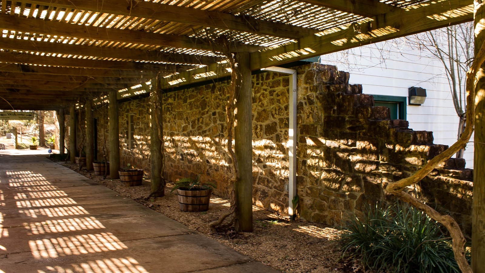A concrete path covered with a wooden awning running along a brick wall
