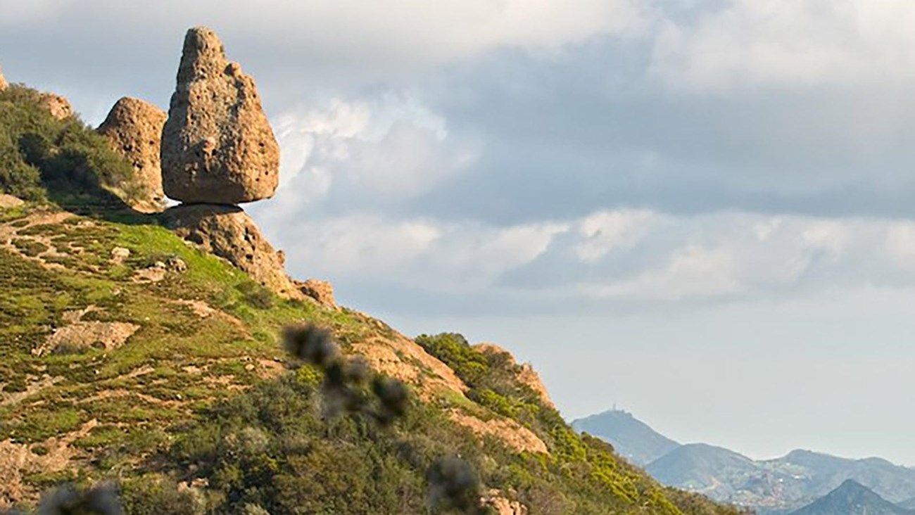 A rock balanced on the side of a mountain.