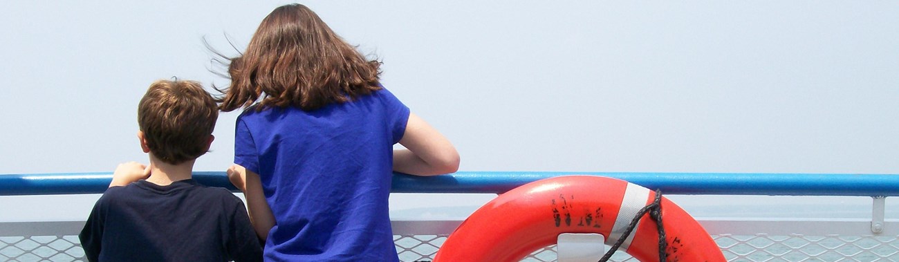 two youth leaning on the gunwale of a boat looking at a broad river