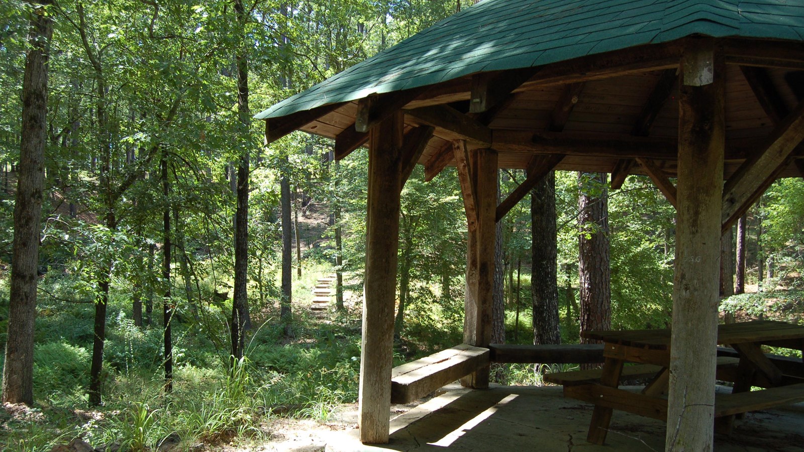 Image of a wooden pavilion with trees surrounding the area. 