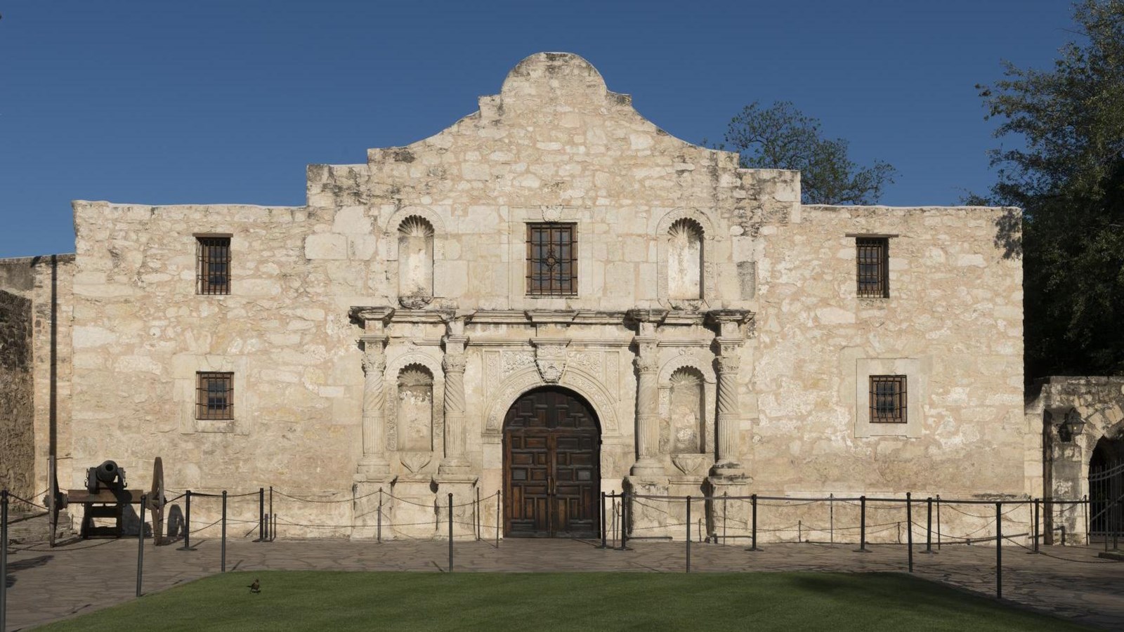 A two-story, stone building with five windows and a wooden door in between four columns