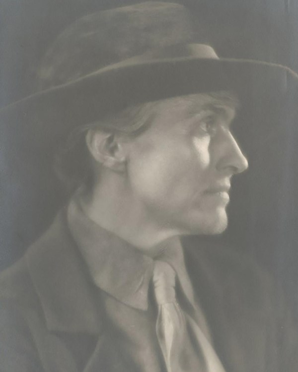 Sepia image of Edna's profile in a suit, tie and hat.