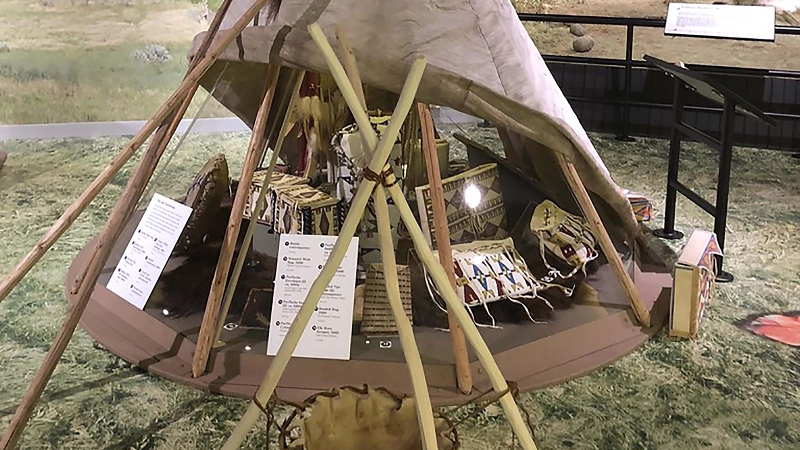 A museum exhibit of a Native American teepee, partial rolled up. Several small artifacts are shelter