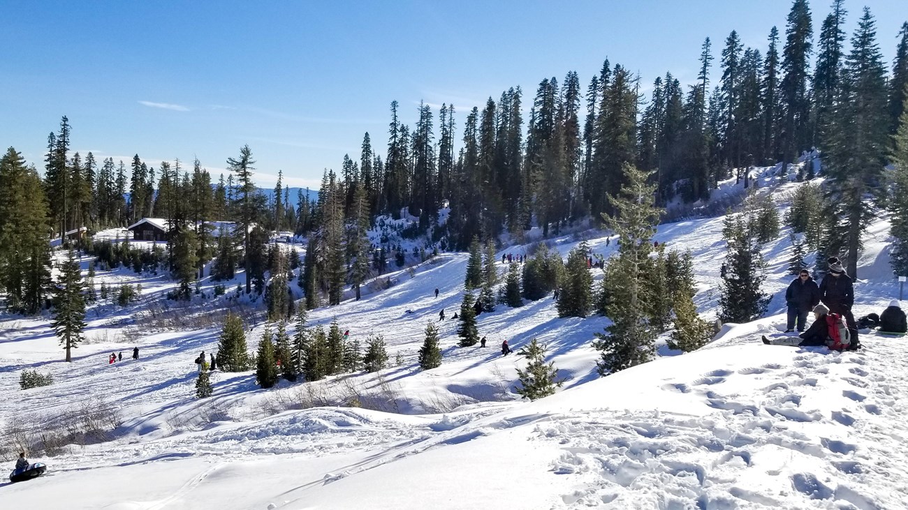 A landscape photo of a snow-covered hill with people playing and a building in the background.