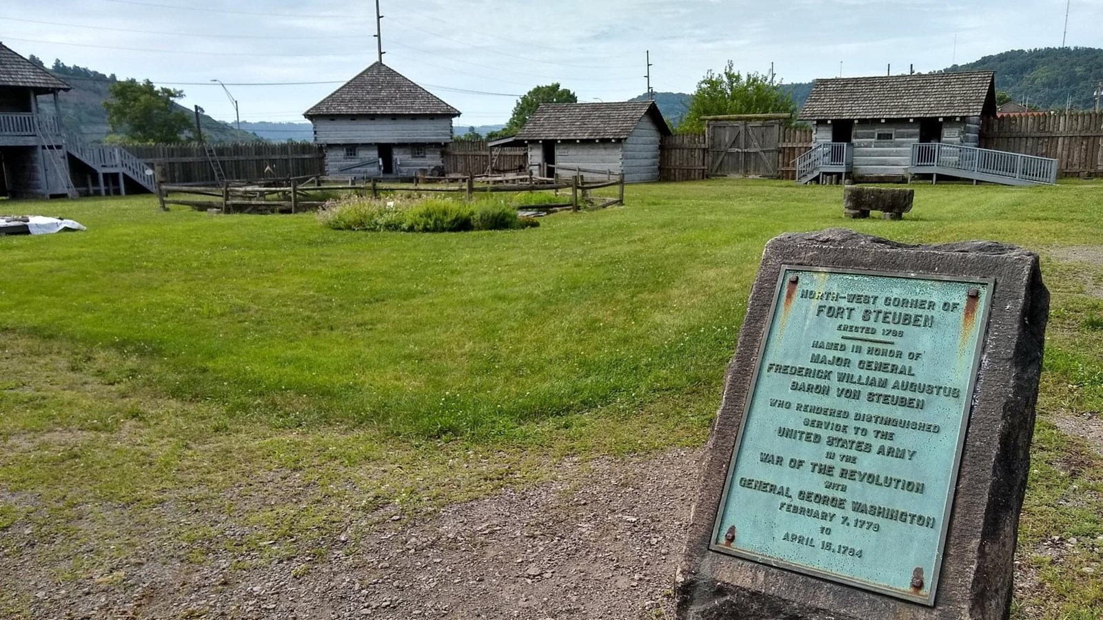 Stone marker for Historic Fort Steuben with wooden fort buildings in the background