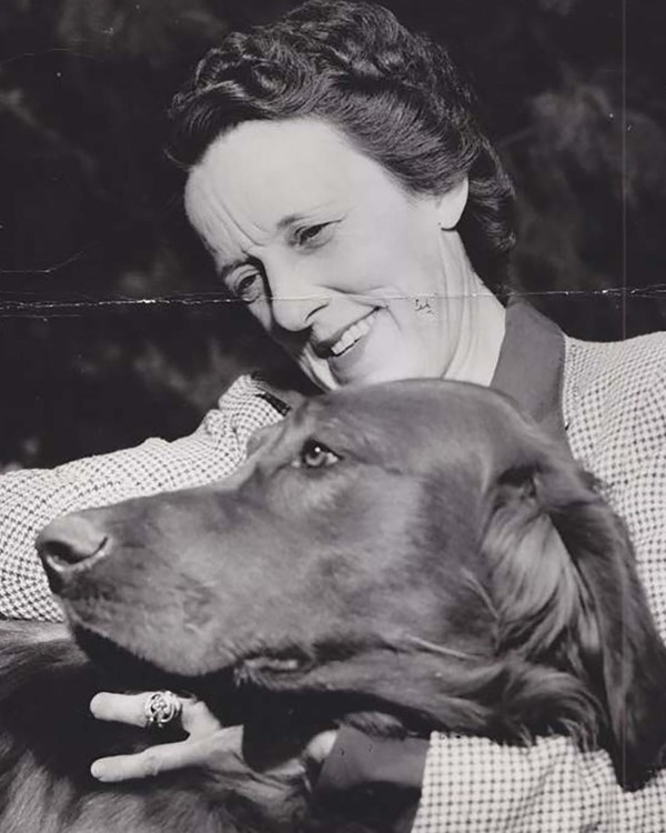 Black and white image of Louise smiling hugging a dog.