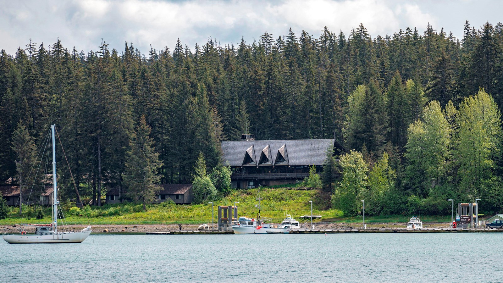 Glacier Bay lodge on the shore, a dock and boats precede it as it sits in a forest.