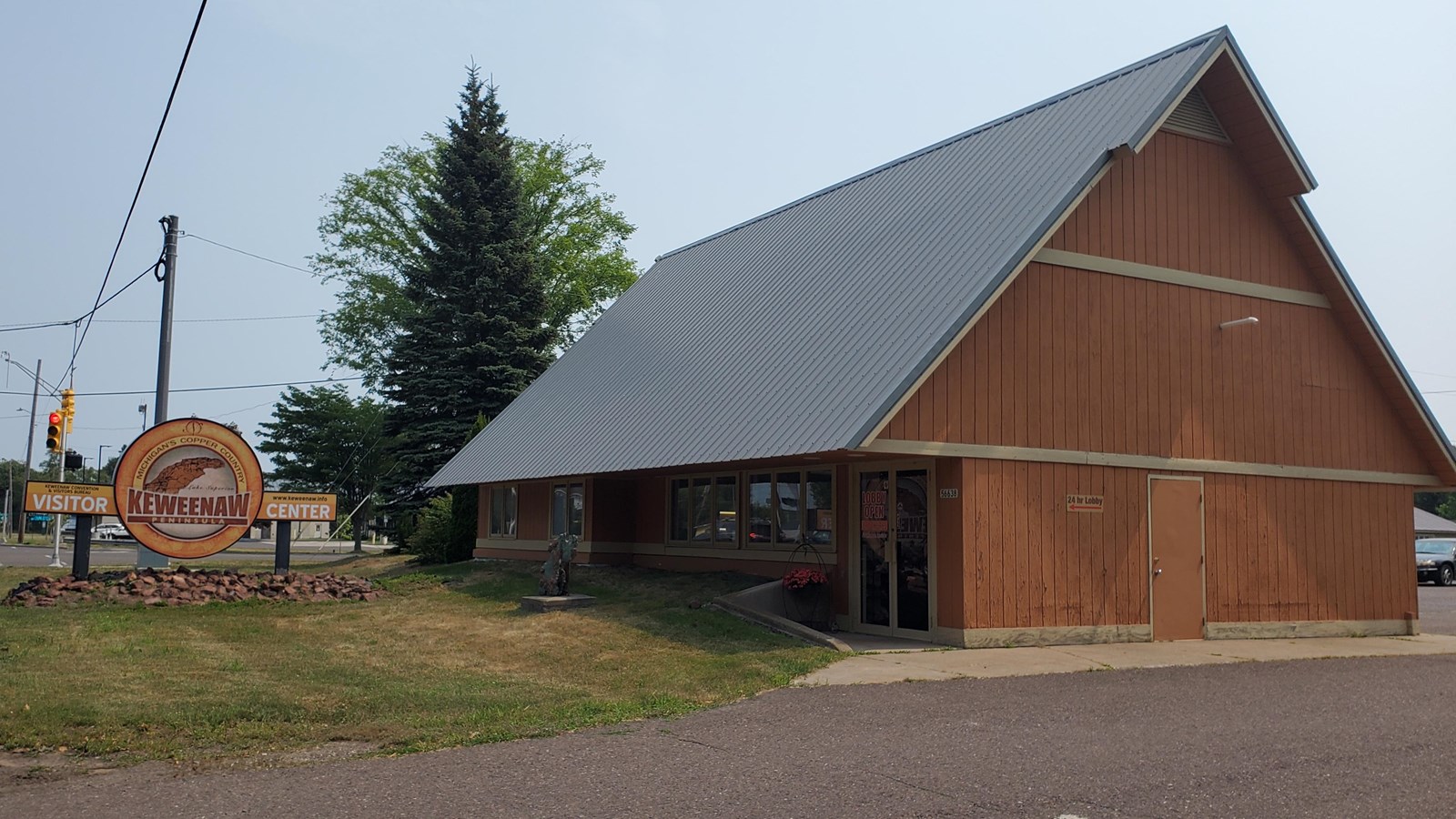 Summer scene with a brown, wooden 2 story A-frame with a steeply pitched roof.