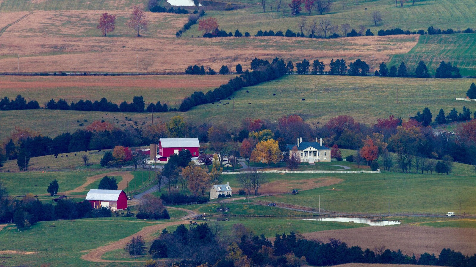 Barns and old plantation buildings among farms on a valley floor are seen from a mountain overlook.