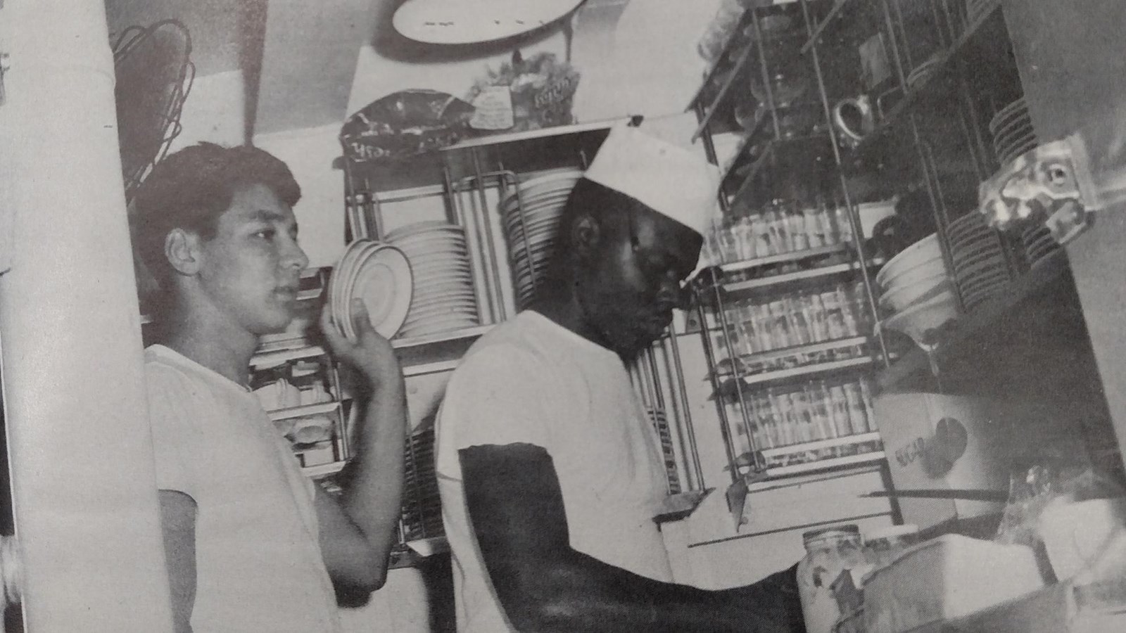 Two stewards in tee shirts and caps work in the pantry of the wardroom.