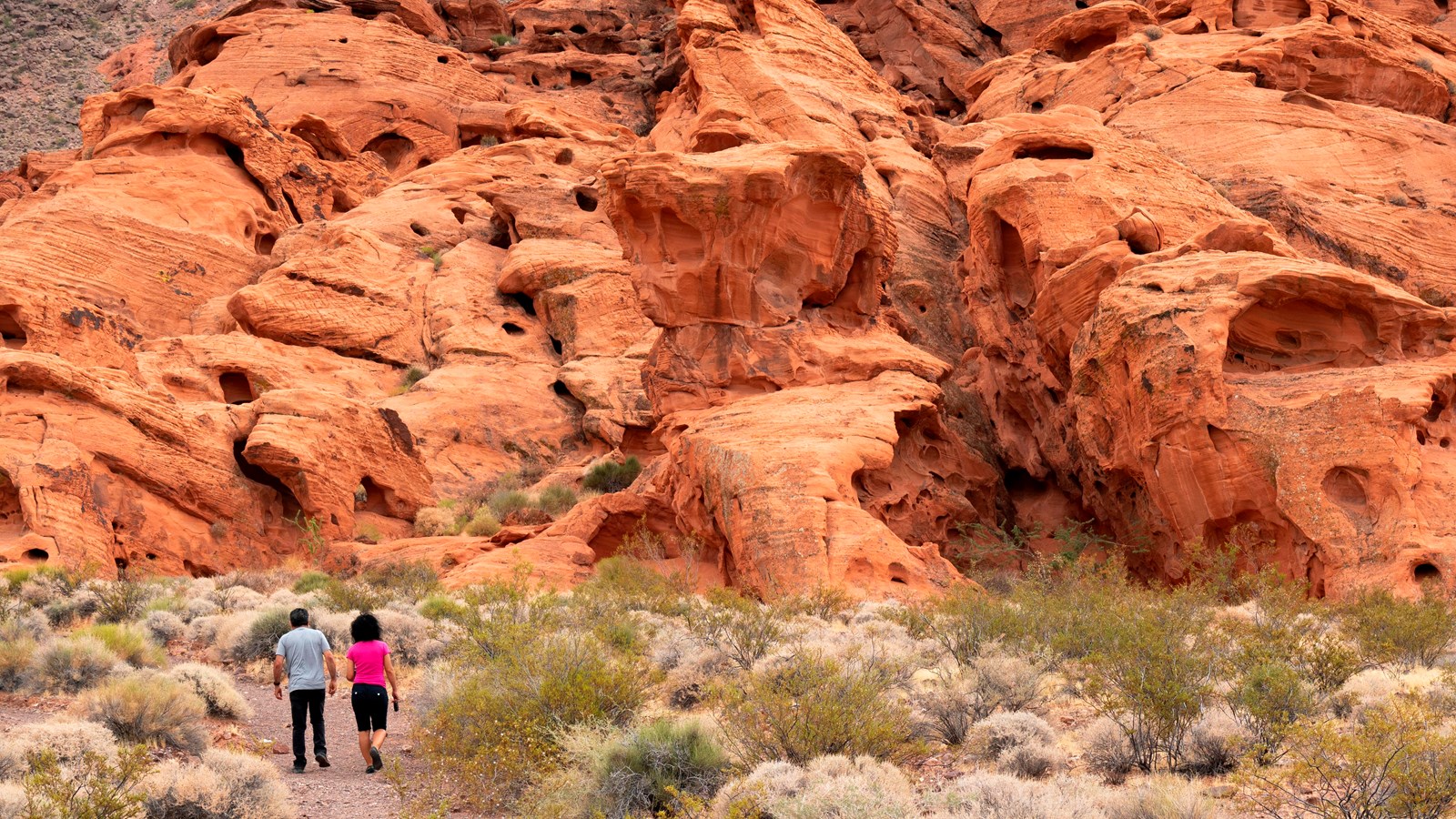Two hikers walking through large redstone features in the desert.