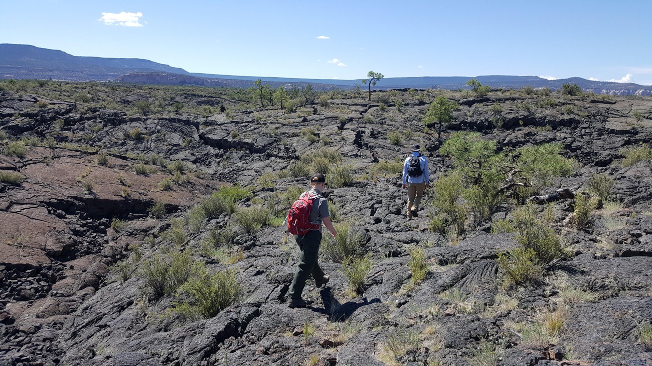 two hikers traverse a rugged trail over black lava rock