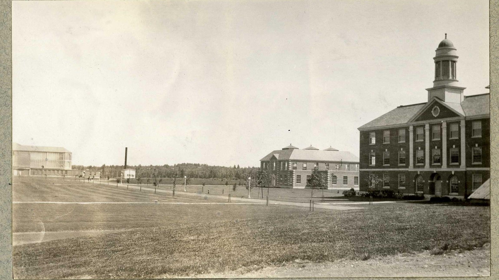 Black and white of buildings around edge of flat grassy area with trees lining paths