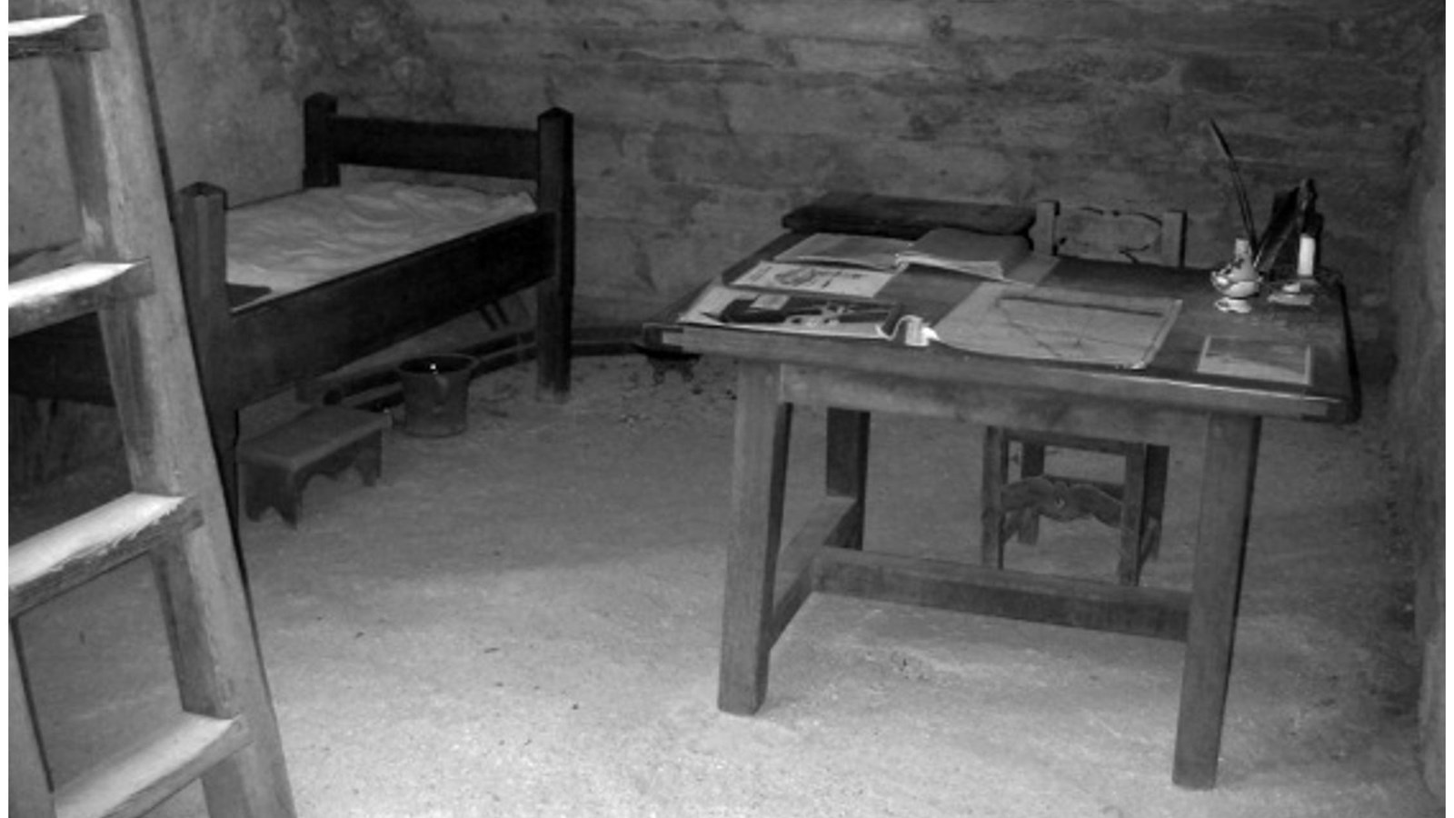 Black & White image showing ladder to roof, bed, and desk