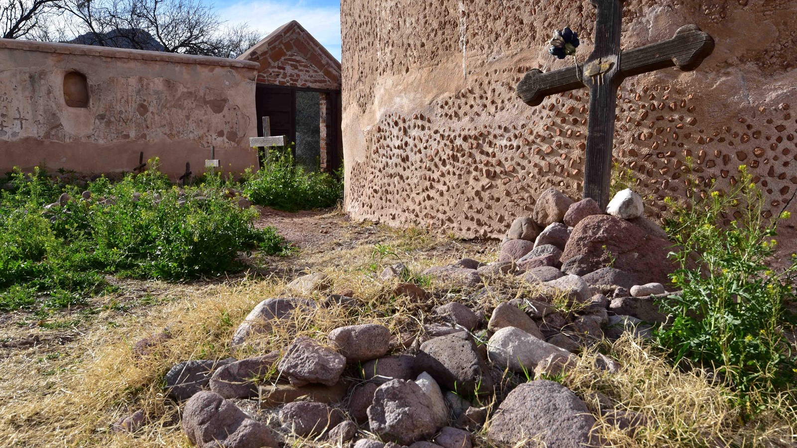 rock-covered gravesite in foreground with round mortuary chapel and gated wall in background